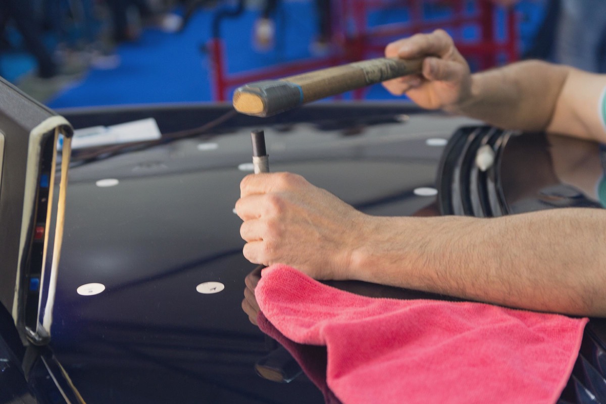 Tecnico che controlla le ammaccature sul cofano di un'auto scura