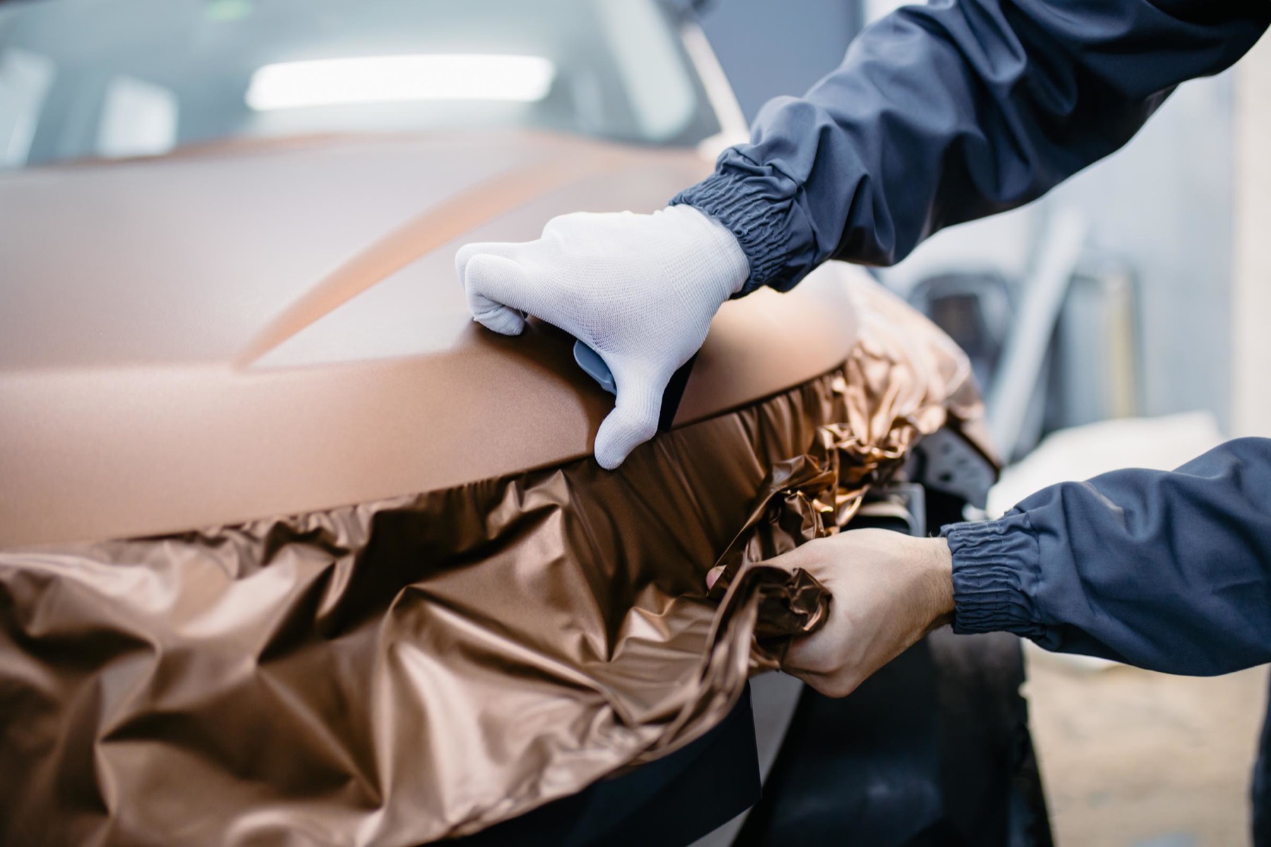 Carrozziere con guanti bianchi che applica una pellicola sul cofano di un'auto