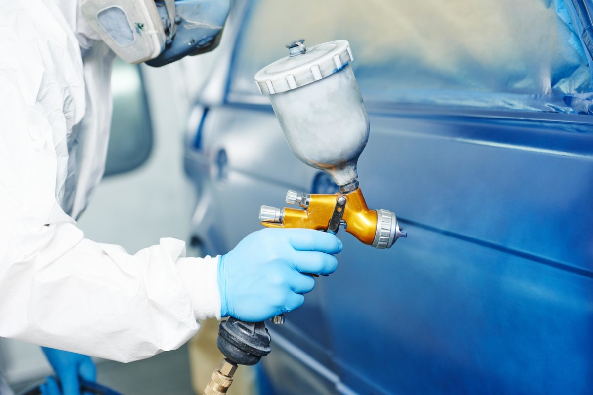 Verniciatore con aerografo al lavoro sulla portiera di un'auto blu